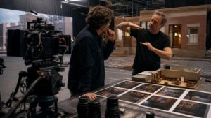 Cinematographer and virtual camera operator planning shot perspective with a camera rig, set model, lenses, and visual frames